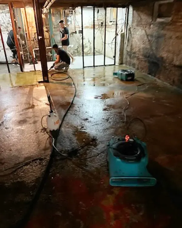 Basement with walls opened to the studs and an air mover drying the wet concrete floor