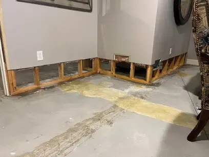 Flood-cut walls along a bare concrete floor drying in an empty finished basement