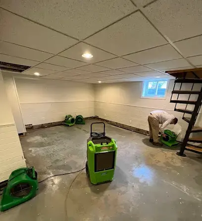 Dehumidifier and air movers drying a finished basement floor while a technician checks the wall