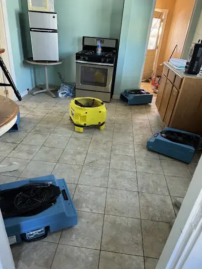 Air movers and a dehumidifier drying the tile floor of a kitchen