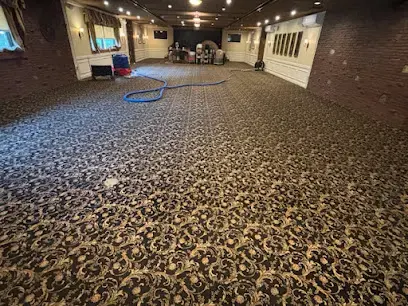 Extraction hose laid across the wet patterned carpet of a long commercial hallway
