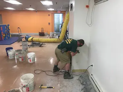 Technician working at the base of a wall while a yellow duct carries dry air into the room